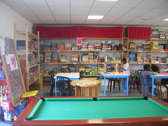 Salle avec une table de billard, des tables et chaises ainsi que des étagères avec de nombreux jeux de société