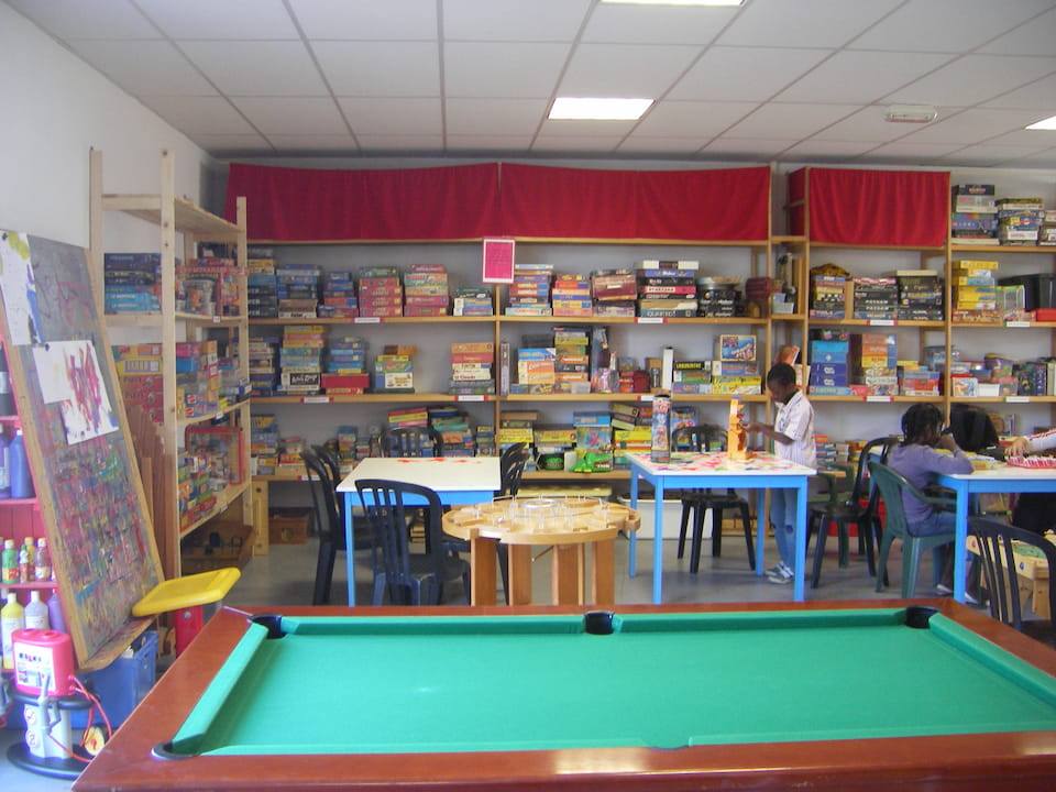 Salle avec une table de billard, des tables et chaises ainsi que des étagères avec de nombreux jeux de société